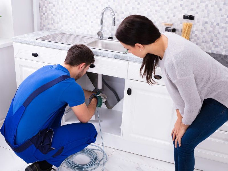 Plumber fixing tap in kitchen for client with client lookin on John G. Plumbing Current Promotions and Rebates