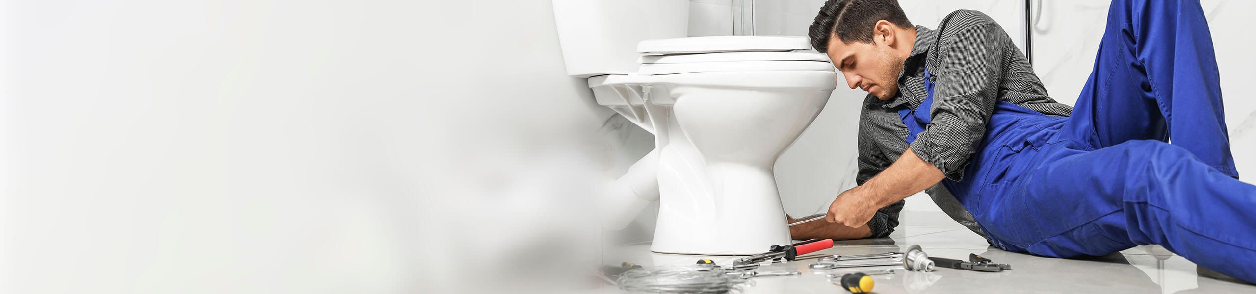 Man laying on bathroom floor replacing a clogged toilet