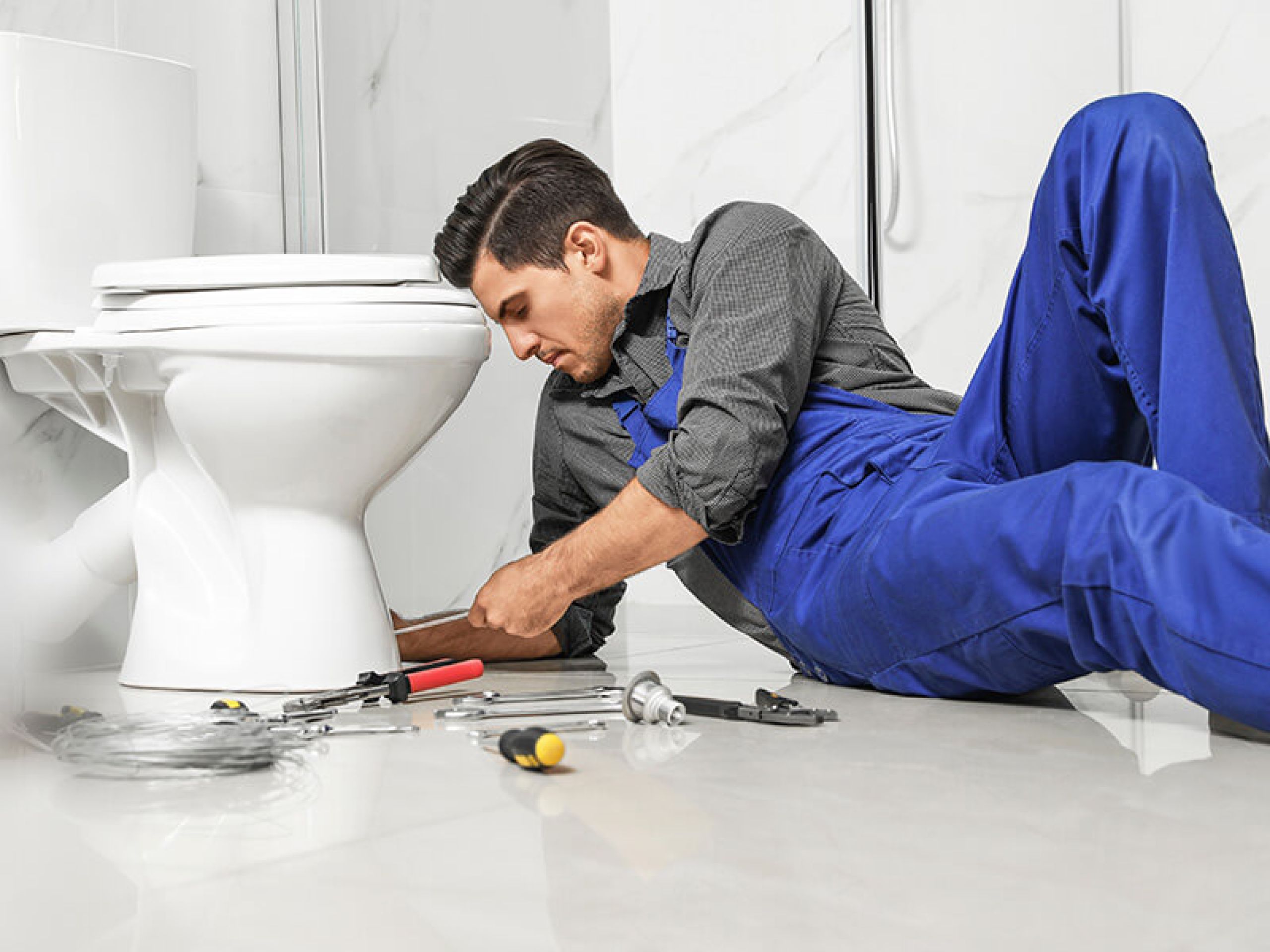 Man laying on bathroom floor replacing a clogged toilet