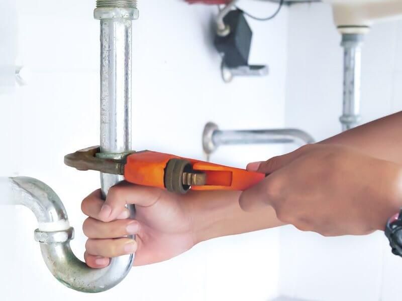 A person holding a wrench and is fixing a pipe.