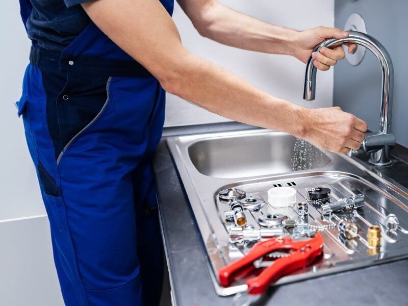 Plumber fixing pipe under sink John G. Plumbing Coombs