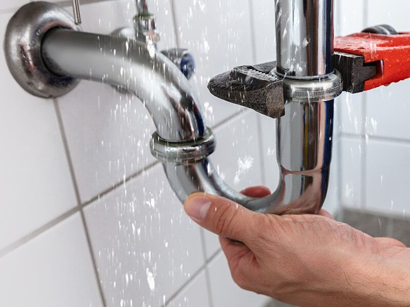 a hand holding a wrench fixing a burst pipe