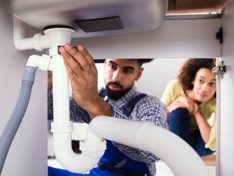Man fixing a pipe under the sink.